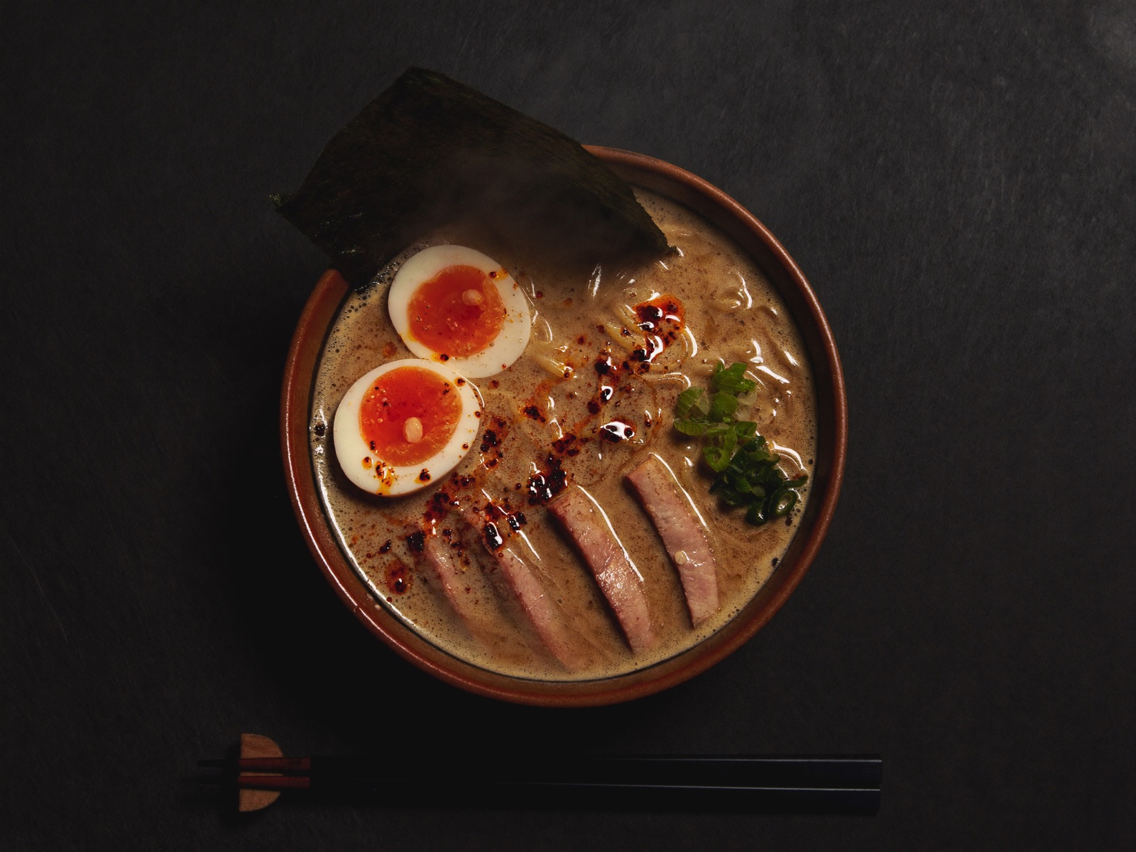 Overhead tonkotsu ramen with coral garnish on dark slate